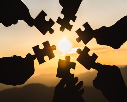 Silhouette  hands connecting  jigsaw puzzle piece against sunrise, Business solutions,  teamwork, partnership, success, goals and strategy concepts.